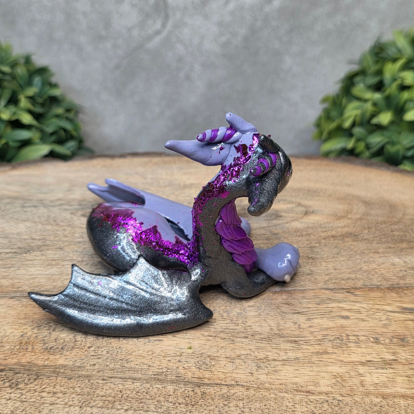 A 2 toned clay dragon sculpture on a wood surface with greenery.