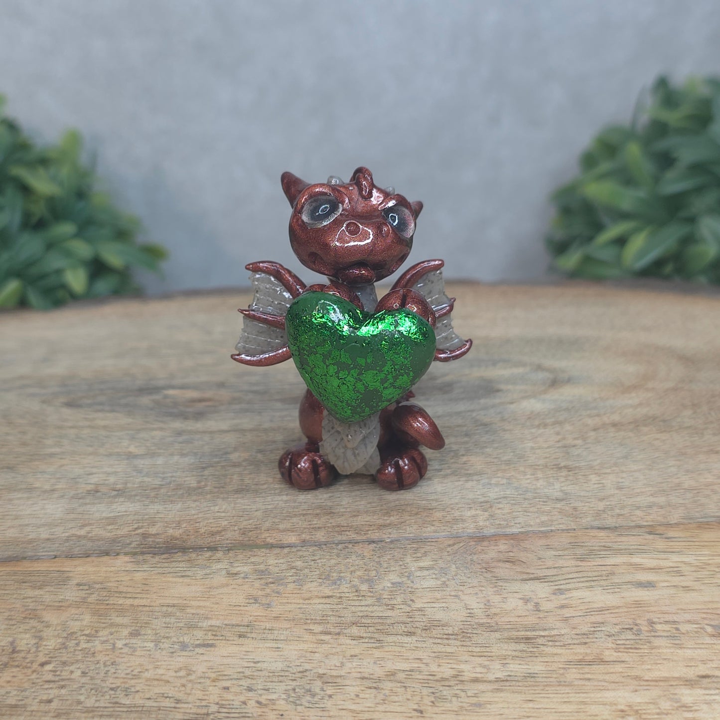 A baby polymer clay dragon with a green heart against a blurred background