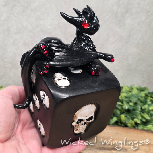 A hand holding a clay dragon on a skull dice