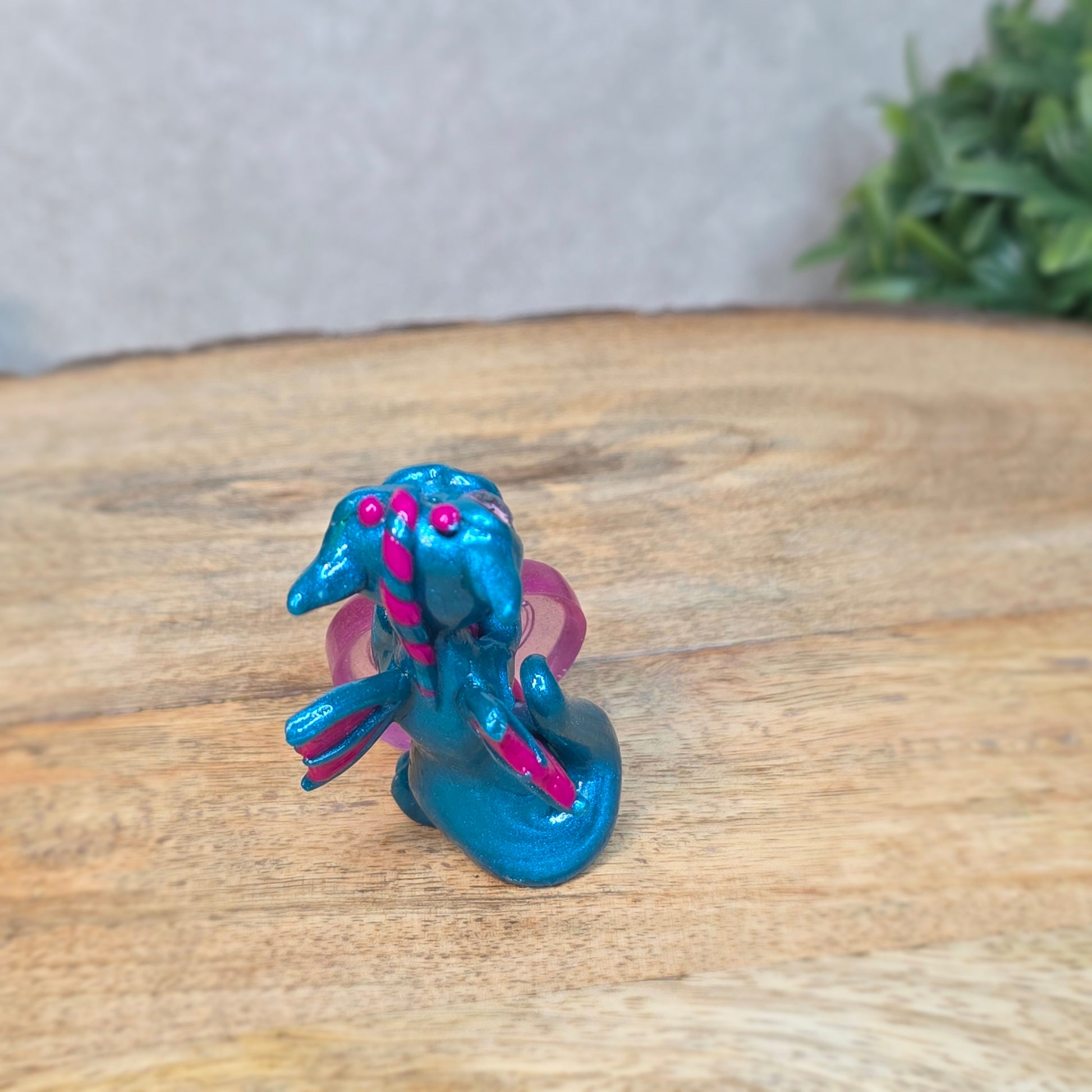 Hand holding a blue and pink clay dragon with a blurred background