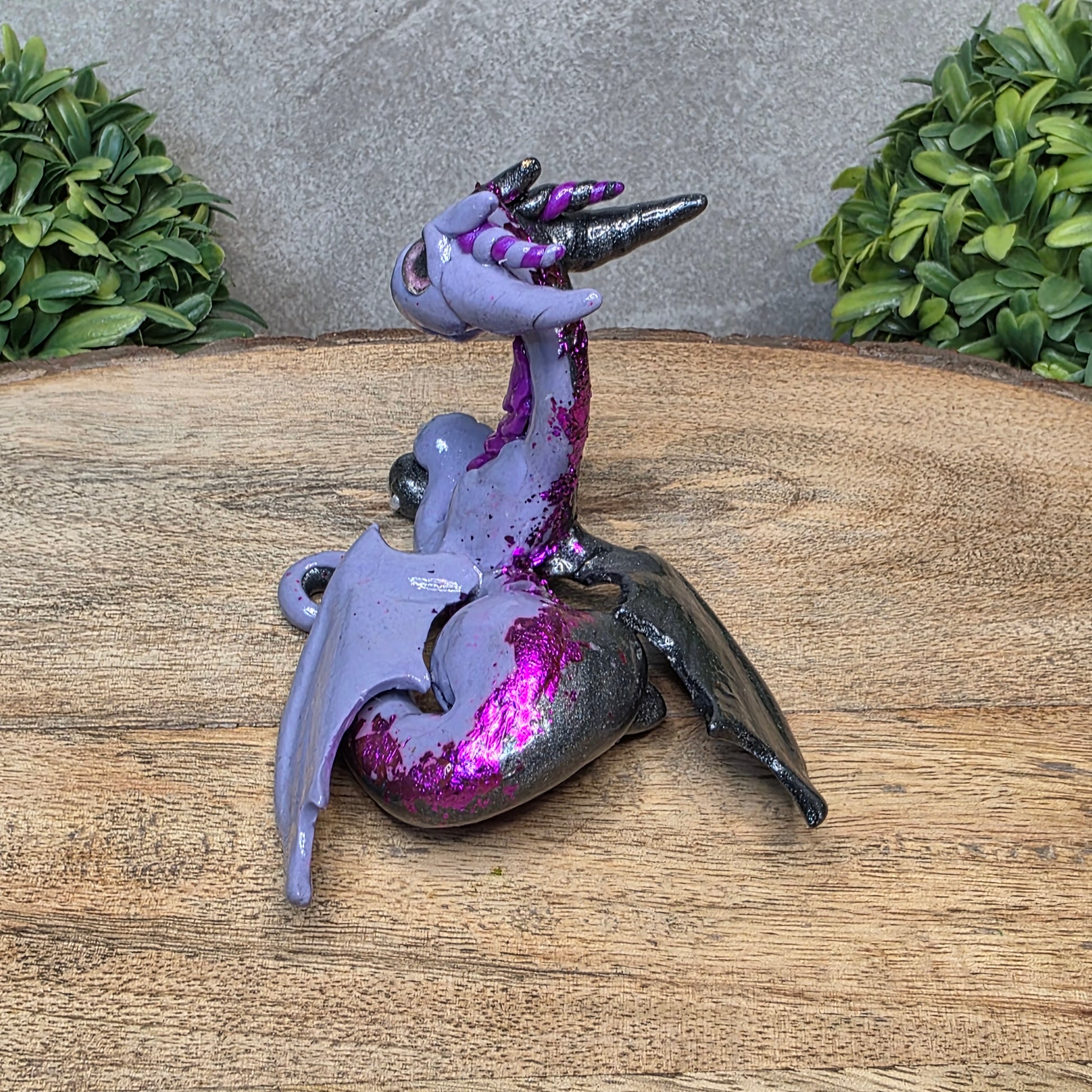 A 2 toned clay dragon sculpture on a wood surface with greenery.