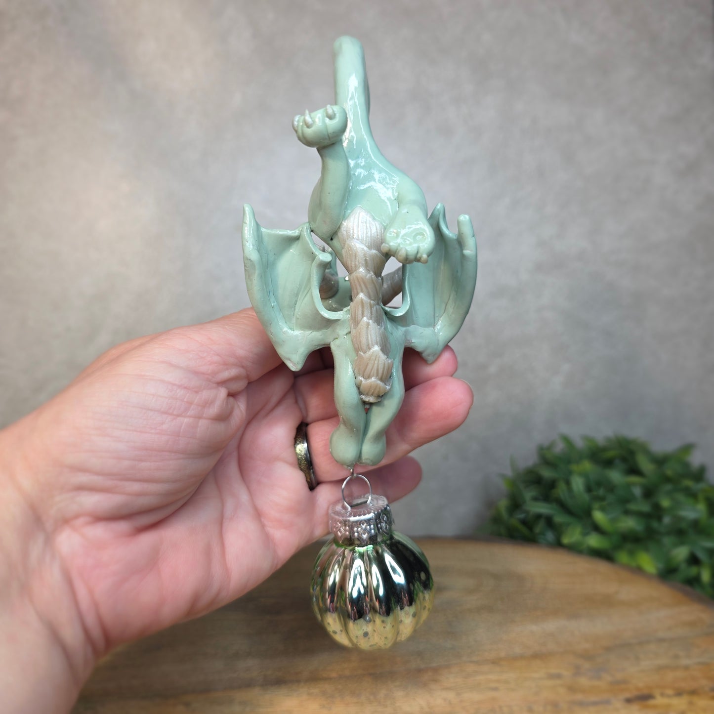 Hand holding a small aqua dragon with glass ornament against a blurred background