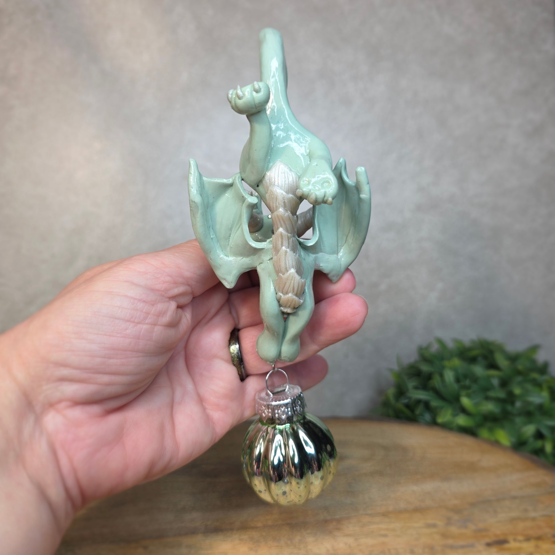 Hand holding a small aqua dragon with glass ornament against a blurred background