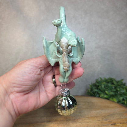 Hand holding a small aqua dragon with glass ornament against a blurred background