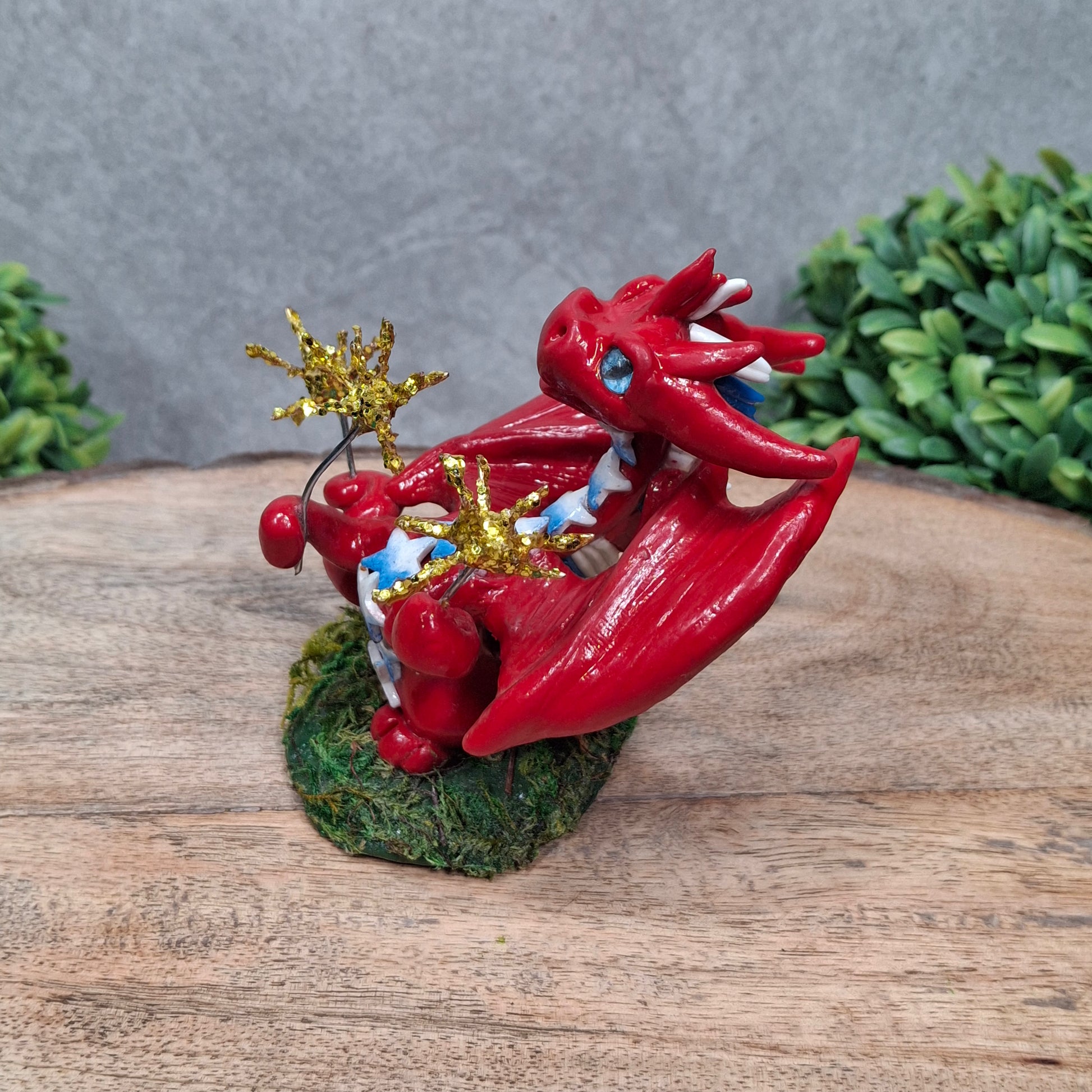 A clay dragon with sparklers against a wood surface with greenery
