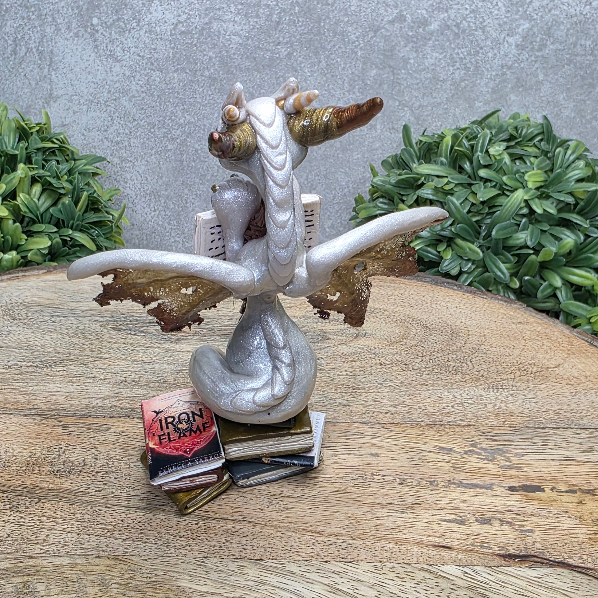 A dragon reading a book against a wood surface with greenery