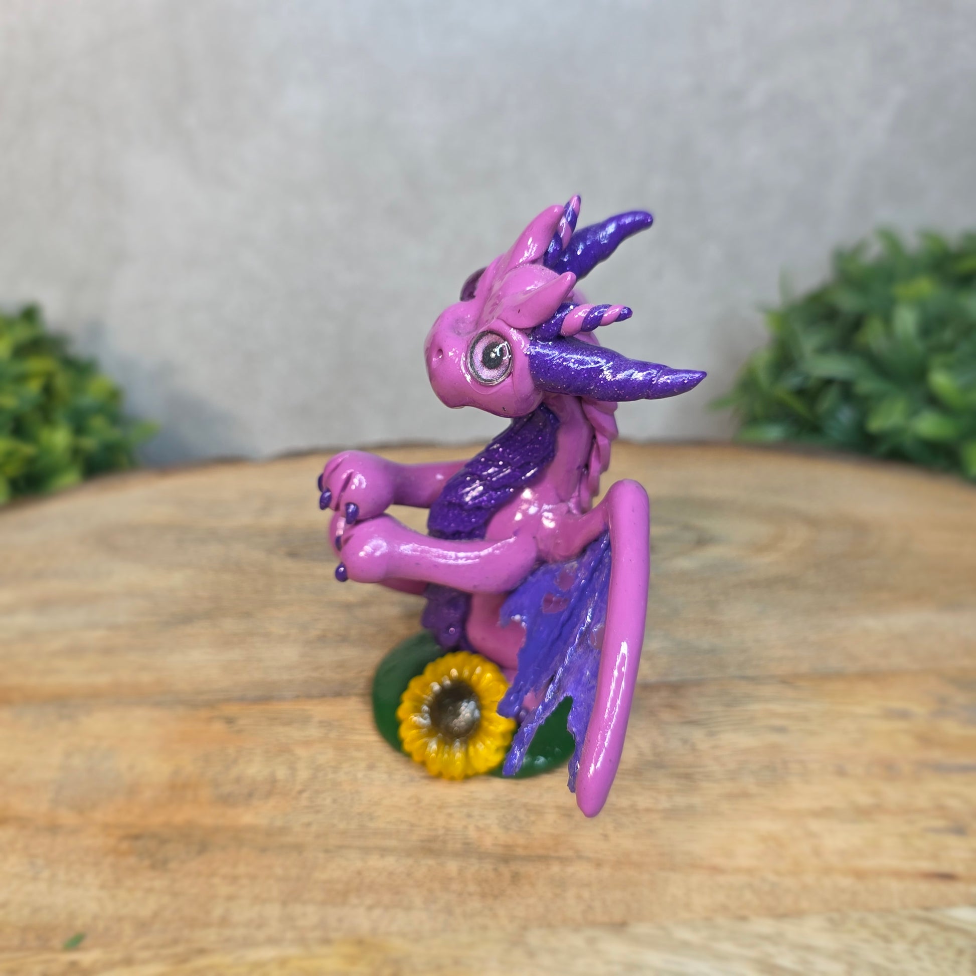 A clay dragon figurine on a wooden surface with a blurred green plant in the background