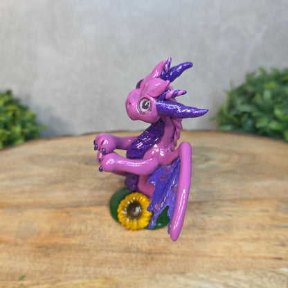 A clay dragon figurine on a wooden surface with a blurred green plant in the background