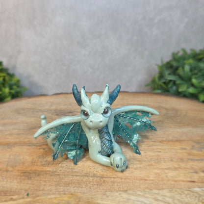 An aqua and turquoise clay dragon against a blurred wood surface