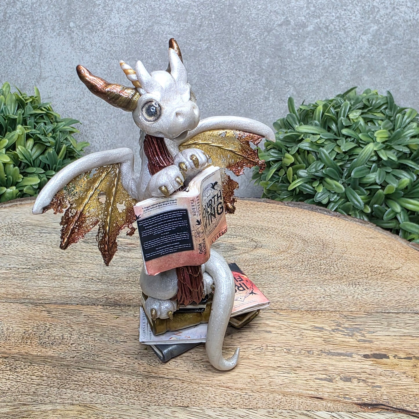 A dragon reading a book against a wood surface with greenery