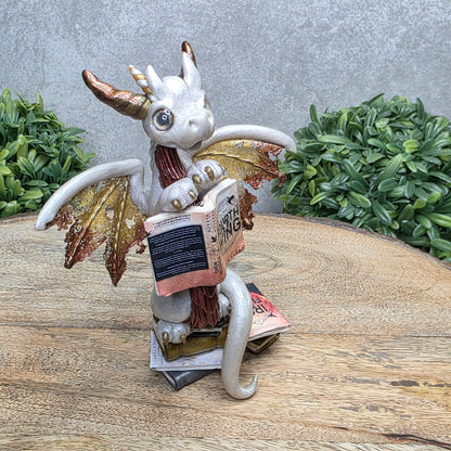 A dragon reading a book against a wood surface with greenery