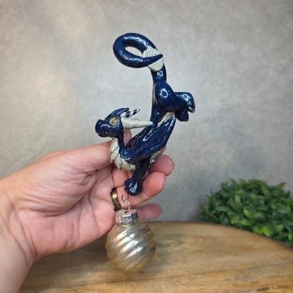 Hand holding a clay dragon with glass ornament against a blurred background
