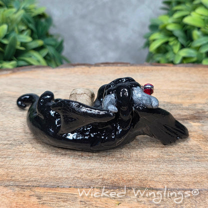 A clay dragon with a skull and potion bottle on a wood surface with greenery. Includes text Wicked Winglings