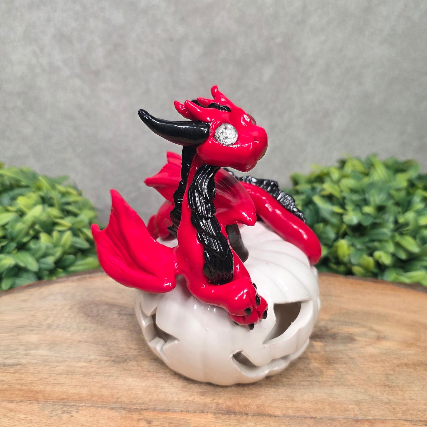 A red dragon sculpture on a white jack o lantern with greenery