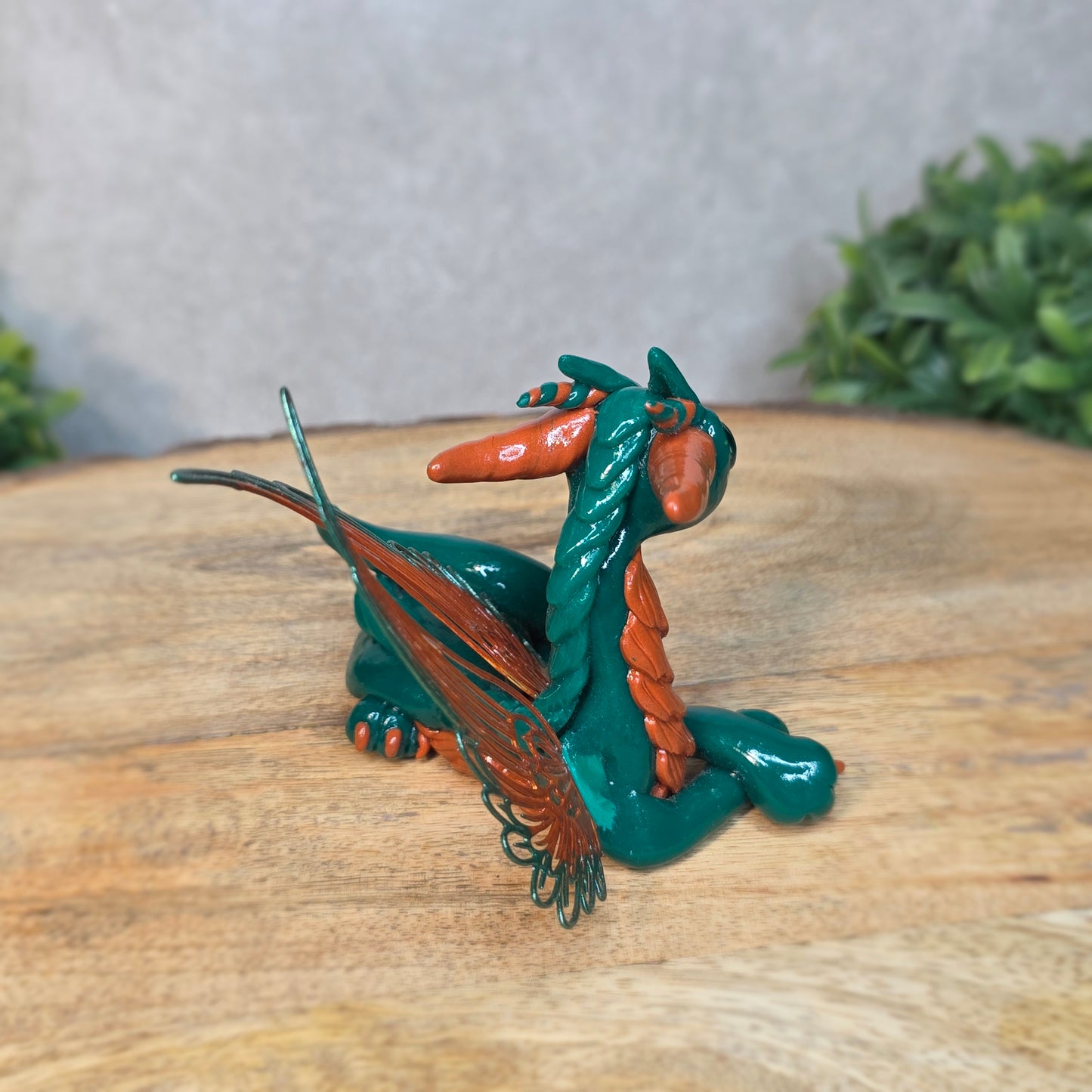 Decorative dragon figurine on a wooden surface with a blurred green plant in the background