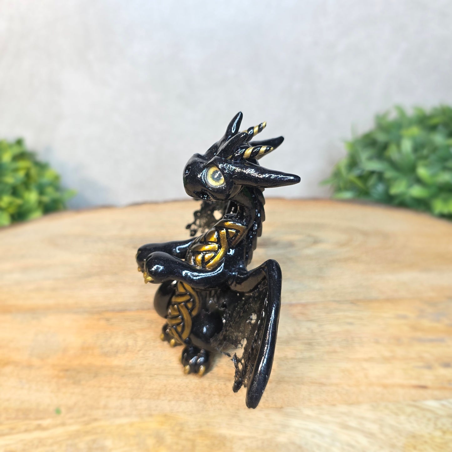 A clay dragon figurine on a wooden surface with a blurred green plant in the background