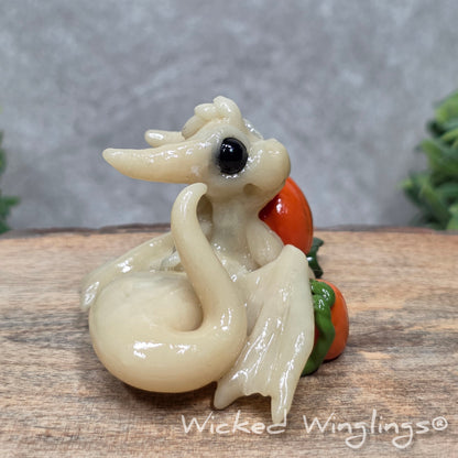 A baby clay dragon sculpture with pumpkins against a wood background with greenery and text Wicked Winglings