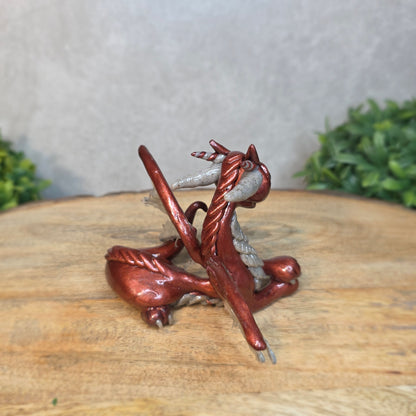 A bronze and gray clay dragon against a blurred wood surface