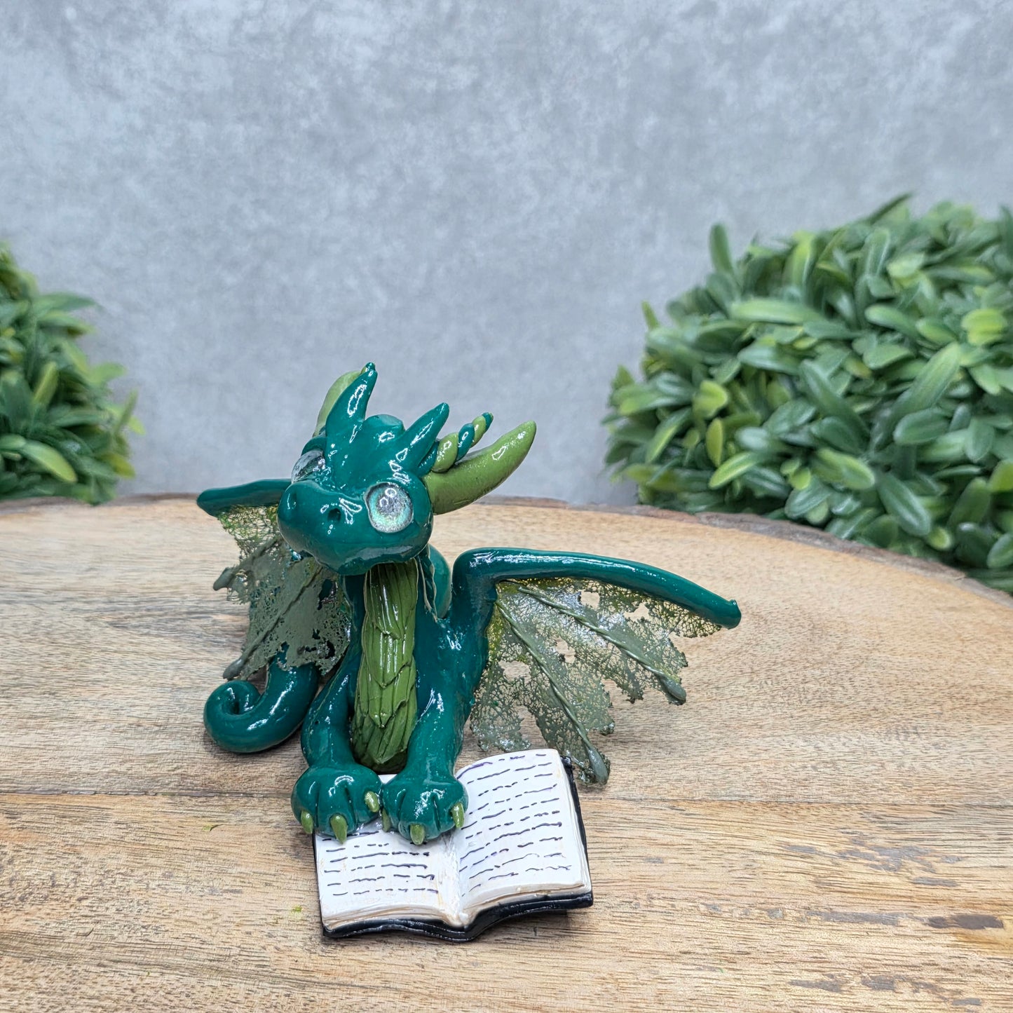 A dragon reading a book against a wood surface with greenery