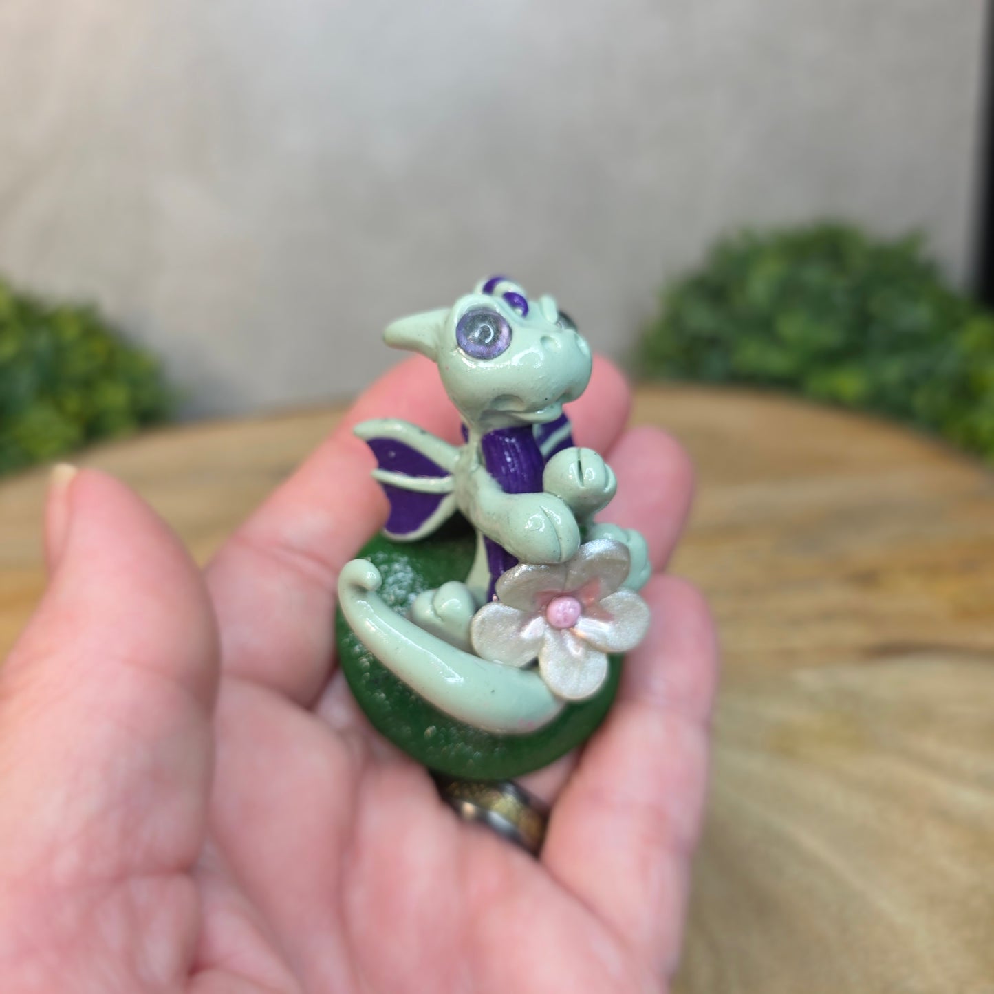 Hand holding a small dragon figurine with flowers against a blurred background