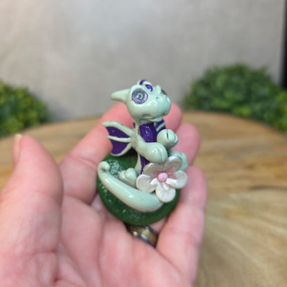 Hand holding a small dragon figurine with flowers against a blurred background