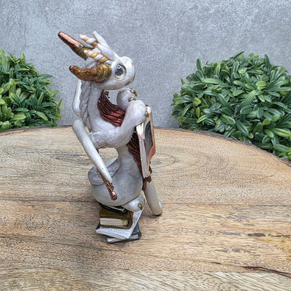 A dragon reading a book against a wood surface with greenery