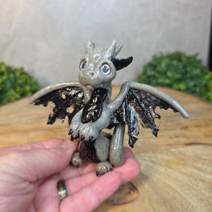 Hand holding a clay dragon figurine with a blurred background