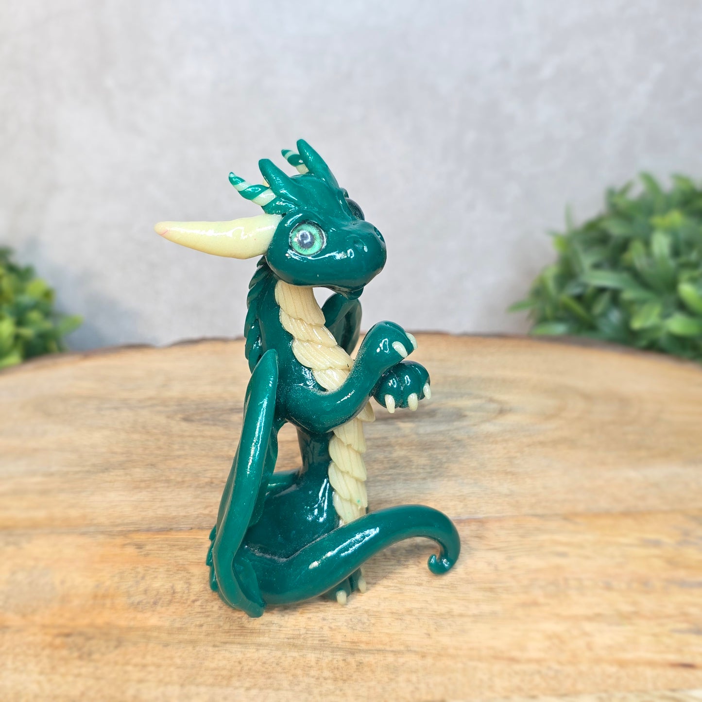 A green and cream clay dragon against a blurred wood surface