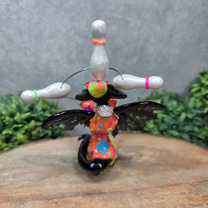 A clown dragon juggling on a wood surface with greenery