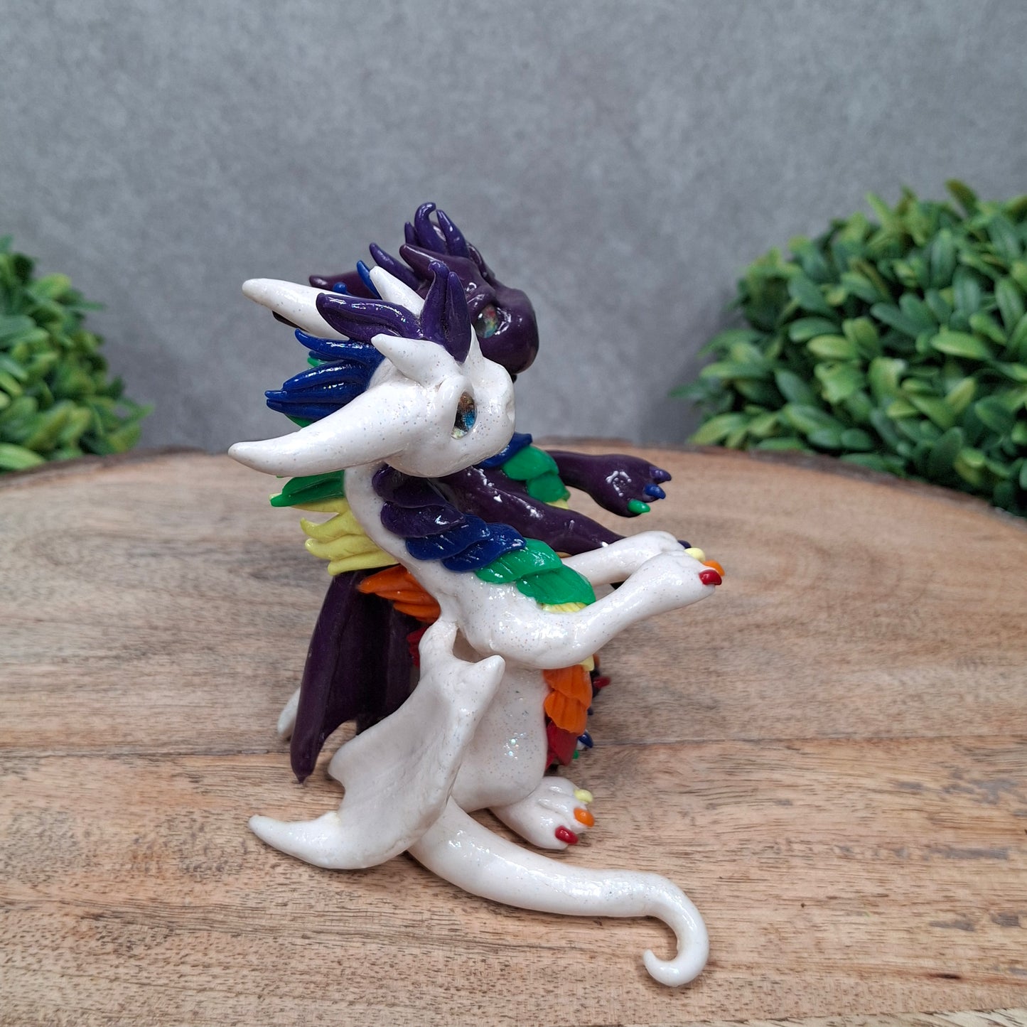a dragon pair with rainbow accents against a wood surface with greenery
