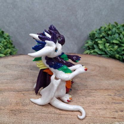 a dragon pair with rainbow accents against a wood surface with greenery