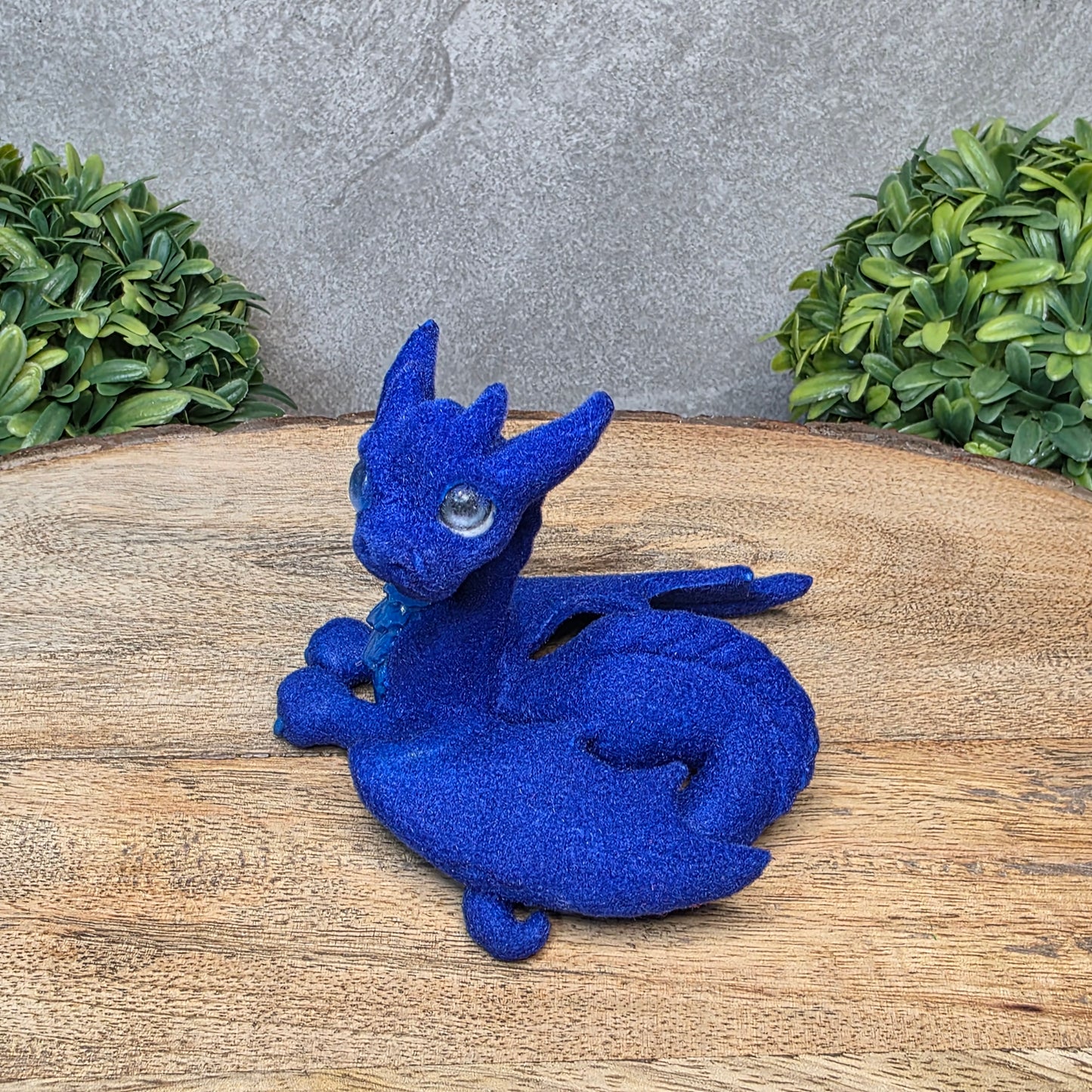 A flocked clay dragon sculpture on a wood surface with greenery.