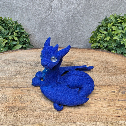 A flocked clay dragon sculpture on a wood surface with greenery.