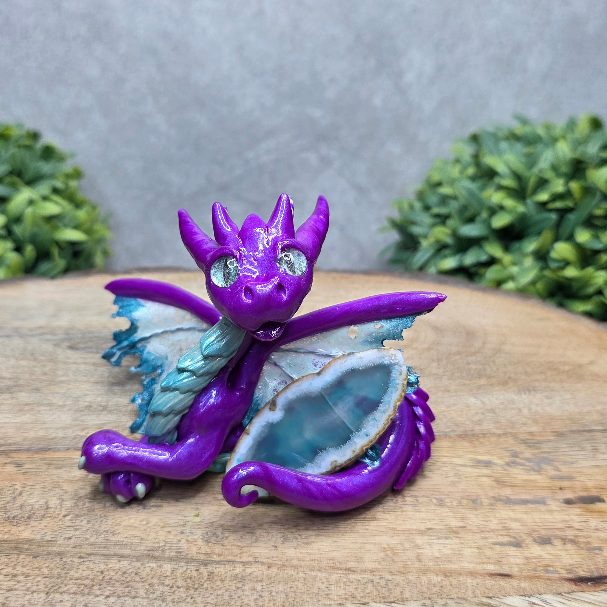 A clay dragon with an agate slice against a wood surface with greenery.