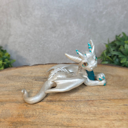 A white and teal clay dragon against a blurred wood surface