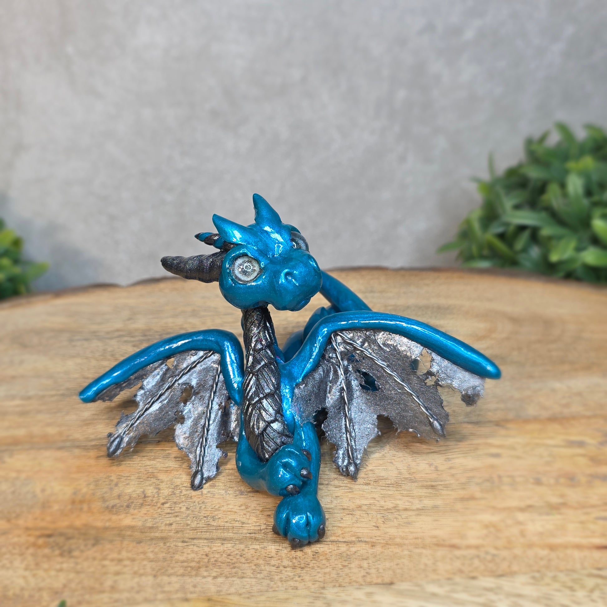 A blue and graphite clay dragon against a blurred wood surface