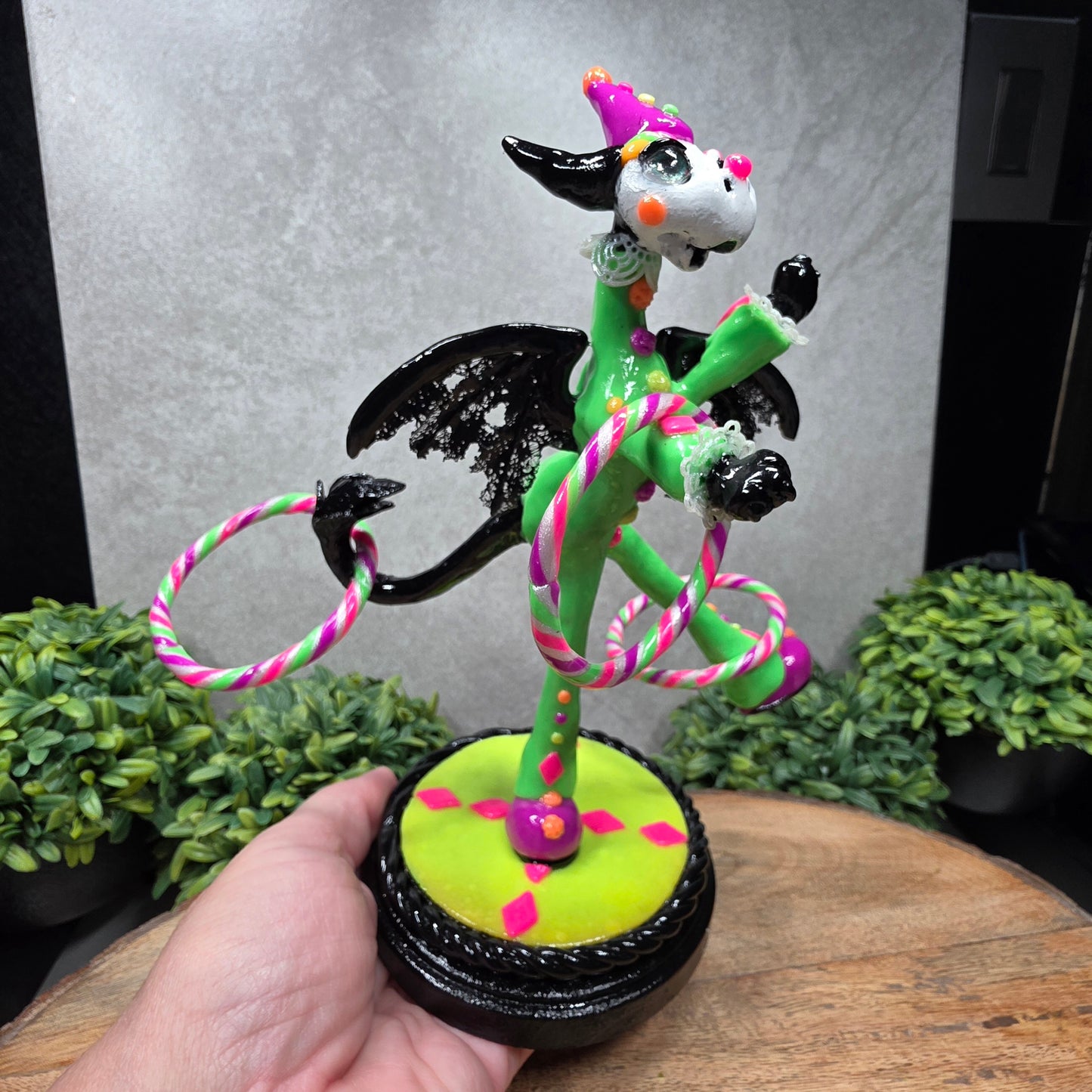 A clown dragon with hoola hoops on a wood surface with greenery