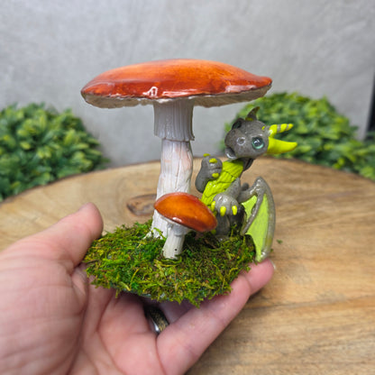 Hand holding a small dragon figurine on a mushroom with a green leafy background