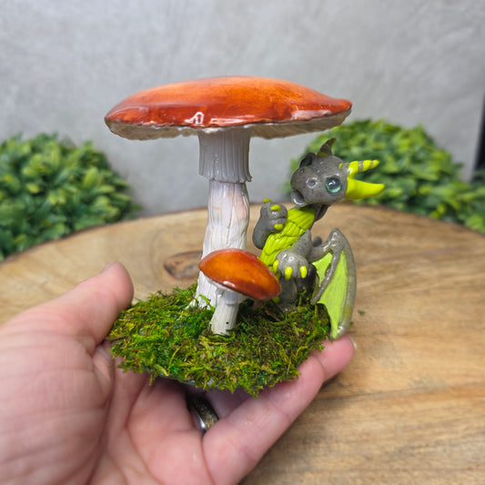 Hand holding a small dragon figurine on a mushroom with a green leafy background