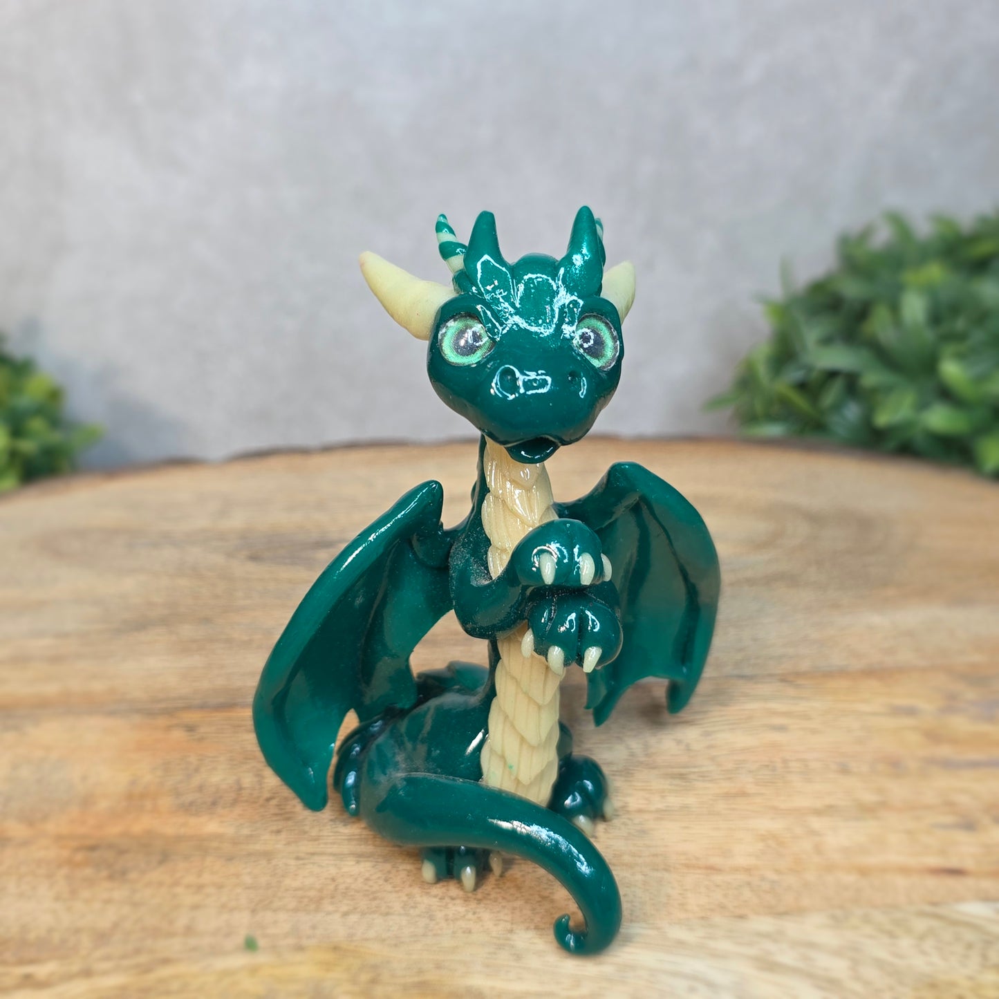 A green and cream clay dragon against a blurred wood surface