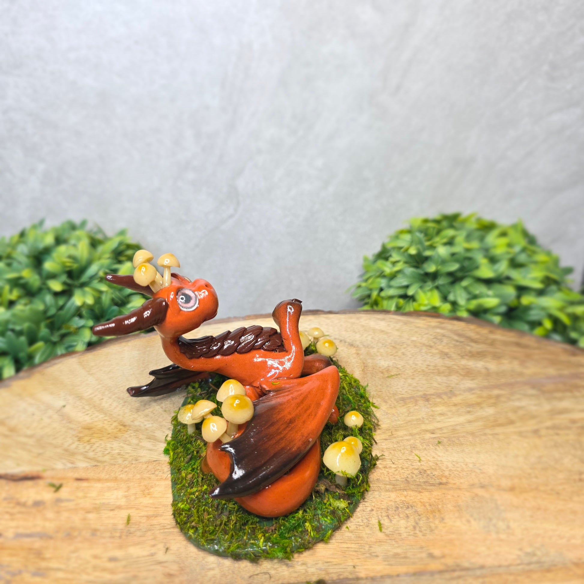 Clay dragon surrounded by mushrooms and moss against a wood background