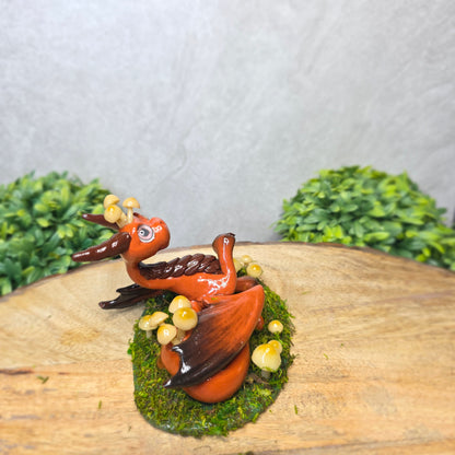 Clay dragon surrounded by mushrooms and moss against a wood background