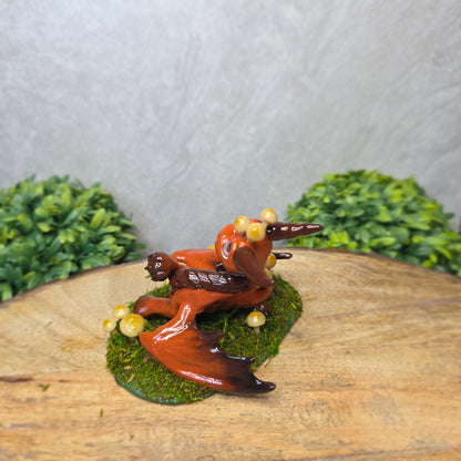 Clay dragon surrounded by mushrooms and moss against a wood background