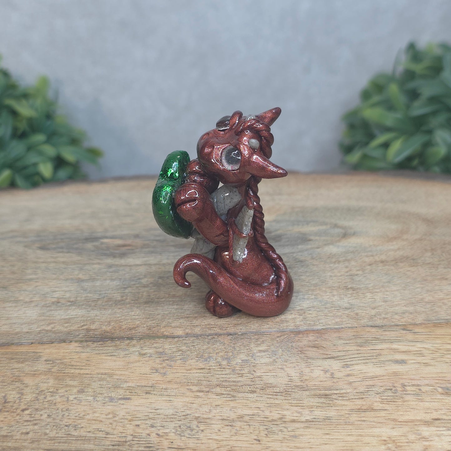 A baby polymer clay dragon with a green heart against a blurred background