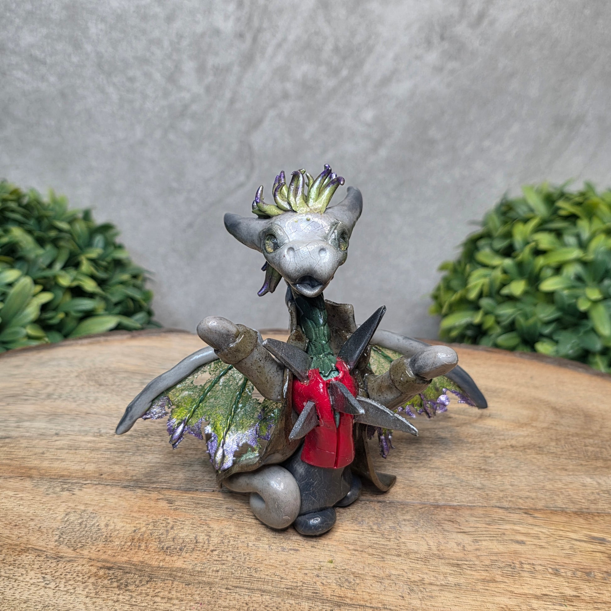Clay dragon in costume on a wood surface with greenery.
