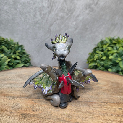 Clay dragon in costume on a wood surface with greenery.