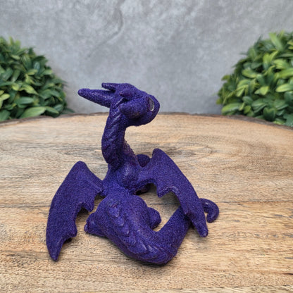 A flocked clay dragon sculpture on a wood surface with greenery.