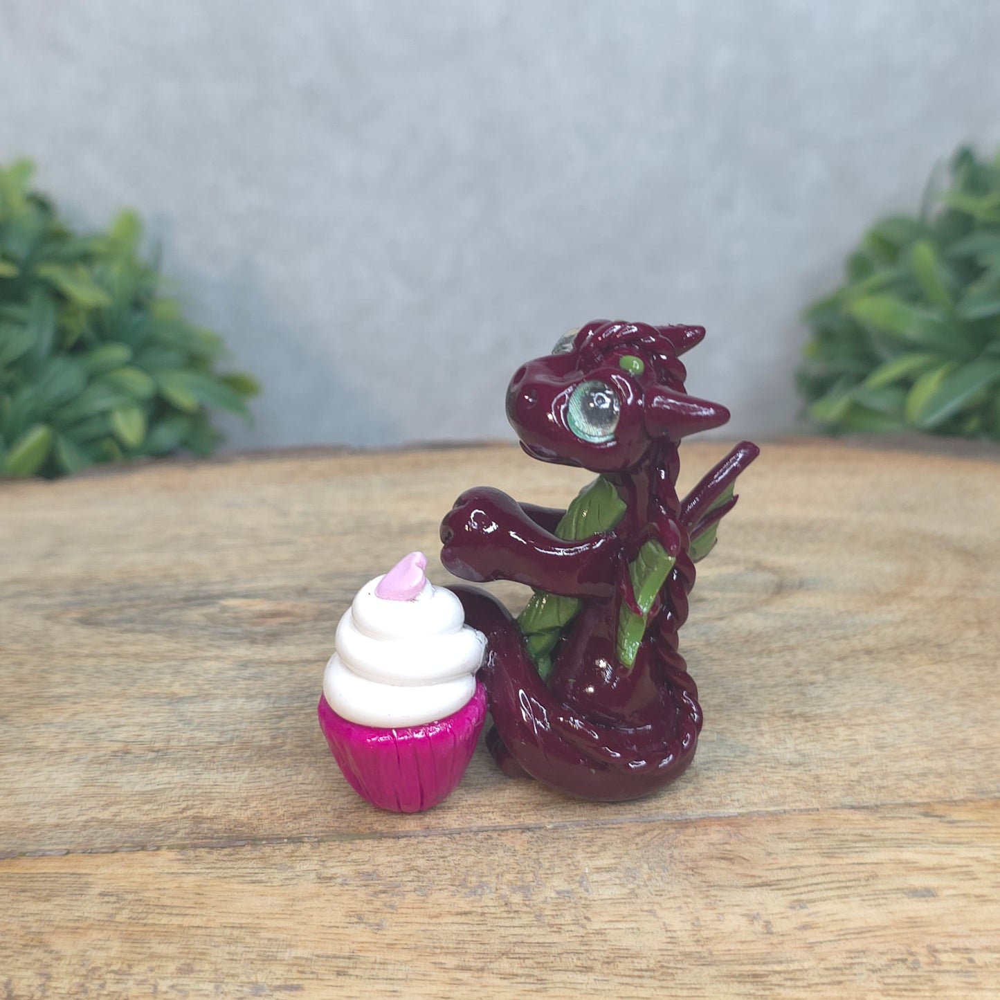 A baby polymer clay dragon with a cupcake against a blurred background