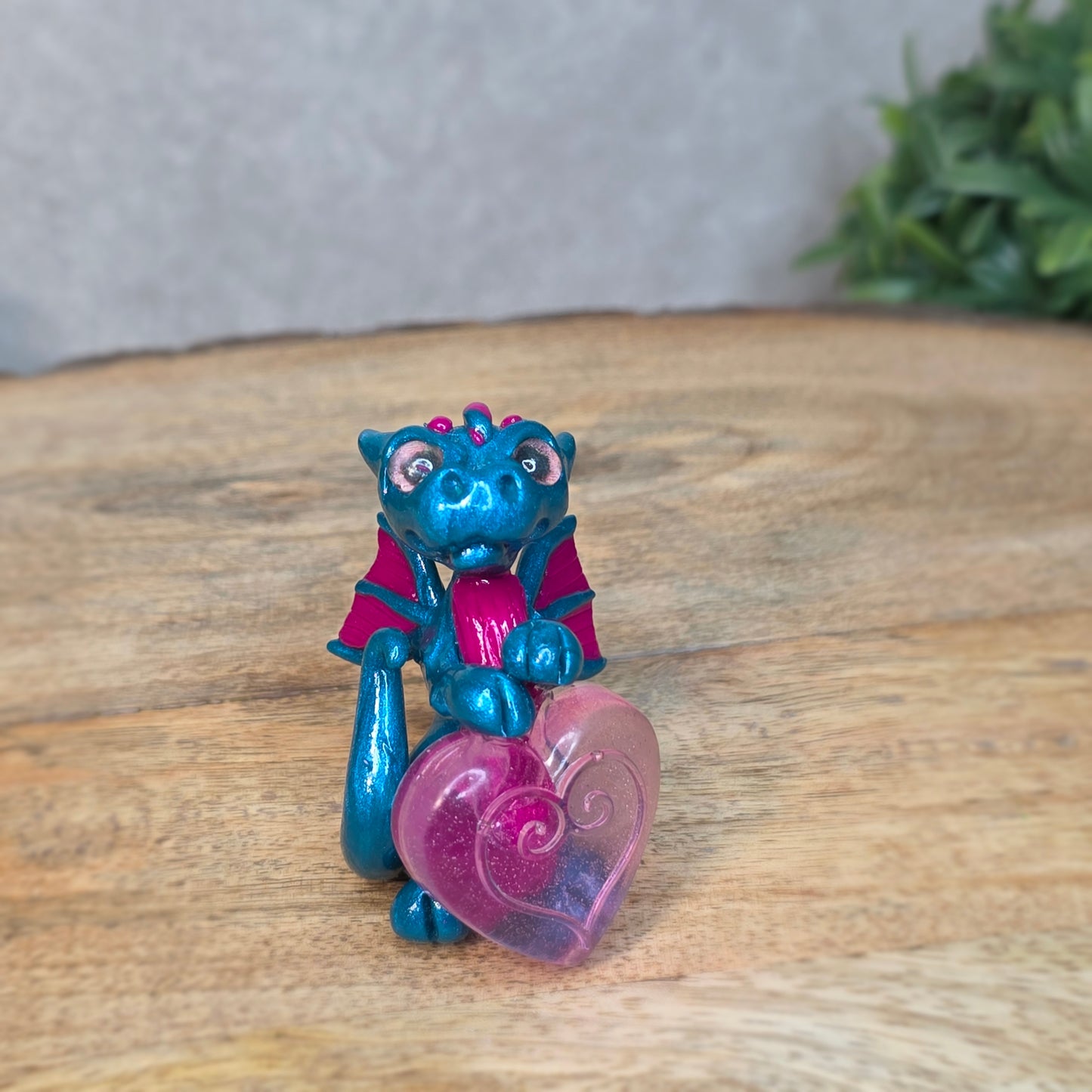 Hand holding a blue and pink clay dragon with a blurred background