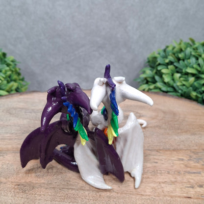 a dragon pair with rainbow accents against a wood surface with greenery